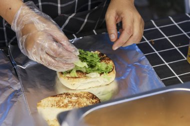 Profesyonel mutfakta yemek hazırlarken eldiven şefinin elini kapat. Kızarmış ekmeğin üzerinde marullu taze burger ya da sandviç yapmaya odaklanmış.