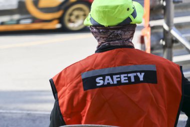 Turuncu yelek ve sert şapkalı profesyonel işçinin arka görüntüsü. İş yerinde iş güvenliği, koruma, güvenlik ve risk yönetimini temsil eden bir sanayi çalışanı