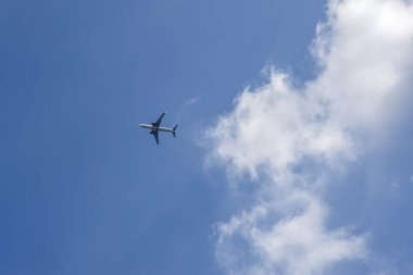 Uçan bir uçağın engin mavi gökyüzünde beyaz bulutlu görüntüsü seyahat, seyahat, özgürlük ve verimli bir ulaşım hissi uyandırıyor.