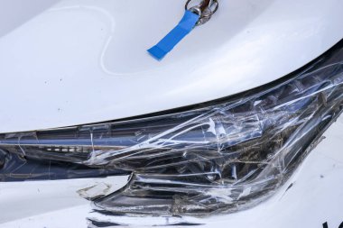 Frustrating close up of broken white car headlight with damage from an accident. vehicle part covered with plastic and tape shows temporary repair needed after crash