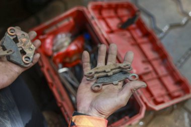 Tamir ve bakım sırasında arabanın kirli fren yastığını tutan odaklı tamirci eli. Arka planda araç kutusu olan eski bölümü kontrol eden bir otomotiv profesyoneli