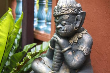 Huzurlu Asyalı muhafız iblis heykeli, mitoloji ve kültürü temsil eden ruhani heykel, sakince bahçede oturur. yıpranmış figür dingin ifadeyi gösterir