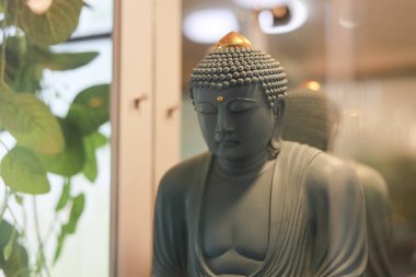 Huzurlu gri Buda heykeli meditasyonda. Bu sakin, ruhsal Asya heykeli kapalı gözlerle huzur, sükunet ve huzur dolu iç mekanlarda farkındalığı temsil ediyor.