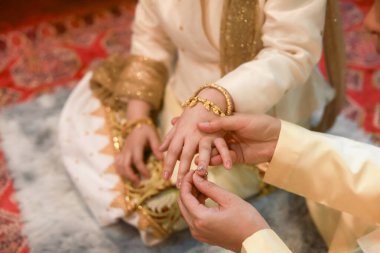 Geleneksel düğün töreninde damadın gelin eline yüzük taktığı hassas bir an. Çiftler için bu kutsal evlilik ritüeli onların derin aşk ve bağlılığını simgeliyor.