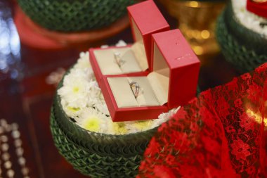 Geleneksel tören için kırmızı kutuda iki alyans. Güzel altın nişan yüzüğü beyaz çiçek tepsisinde, aşkın sembolü, bağlılığın ve kutlamanın.