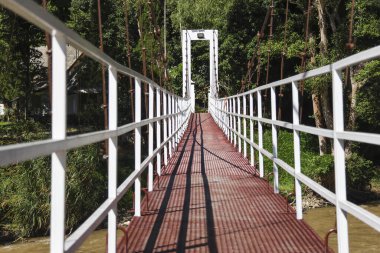 Uzun beyaz metal asma köprü yolu nehrin üzerinden maceralı bir geçiş sağlıyor. Bereketli yeşil ormana ve sakin doğaya açılan yürüyüş yolu perspektifi