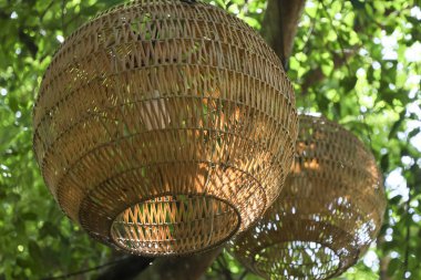 El yapımı bambu fener yeşil bahçedeki ağaçtan sarkıyor. Bu geleneksel, kırsal açık hava dekorasyonu huzurlu ve huzurlu doğal bir arka plan sağlıyor.