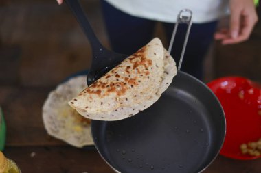 Kahvaltıda kıtır kıtır Hint sosu pişiren kişi. Ev yapımı yemekler siyah tavadan dikkatlice çıkarıldı. Sıcak mutfakta spatula ile lezzetli geleneksel yemekler hazırlandı.