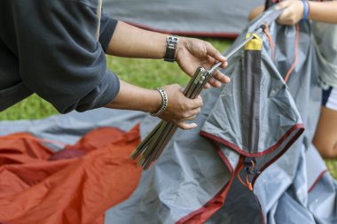 Kamp için çadır kurmaya odaklanmış iki kişi. Eller, yaz aylarında bir açık hava macerası için çim üzerinde sırıkla kumaşı bir araya getirir.