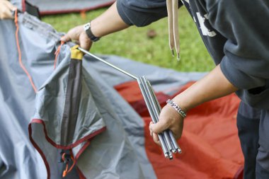 Kamp yaparken, çadır kurma sürecinde odaklanmış bir insan eli. Eğlence, eğlence ve macera için yeşil kamp alanına metal direk yerleştiriliyor.