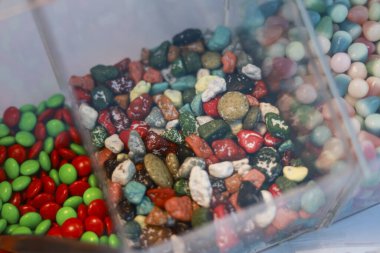 Renkli çikolatalı şekerler ve tatlılar sergileniyor. Şeker kaya ve çakıl taşı şekilleri de dahil bu cazip tatlılar, canlı yiyeceklerin arka planlarını oluşturur.