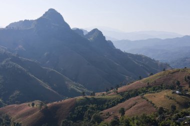 Huzurlu ve heybetli dağ manzarası, sisli vadide belirgin bir tepe noktası. Bu doğal manzara engebeli tepe aralığını gösteriyor. Manzaralı seyahat ve macera için mükemmel bir zemin.