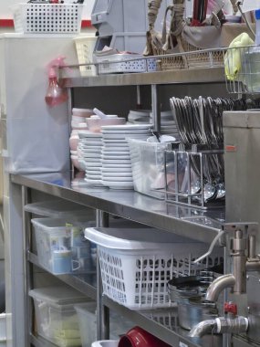 Meşgul bir restoran mutfağının gerçekçi manzarası. Paslanmaz çelik raf temiz beyaz tabaklar, çatal bıçak takımı ve depolama sepetleri servis için hazır.