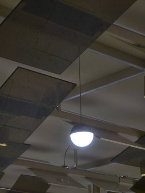 Modern iç tasarım. Askıda asılı ışık geometrik tavanı aydınlatıyor. Lambadan gelen parlak, atmosferik ışık odada sakin, minimalist bir ortam yaratır.