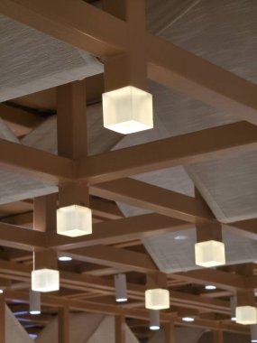 Modern geometrik ahşap kiriş tavanı ve parlayan küp lambaları olan huzurlu ve sıcak mimari iç tasarım her türlü uzay için davetkar ve barışçıl bir ortam yaratır.