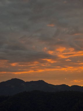 Karanlık dağ siluetinin üzerinde dramatik bulutlu gökyüzü olan huzurlu turuncu gün batımı. Bu dingin ve manzaralı manzara sakin ve güzel bir duygu yaratır.