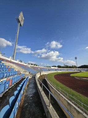 Boş bir stadyum ve atletizm pistinin sakin perspektifi. Mavi koltuk, yeşil alan ve arena parlak gökyüzü altında yarışmayı bekliyor. sessiz arka plan