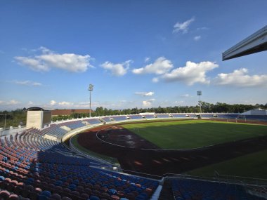 Boş spor stadyumu tribünü yeşil çimen tarlasını görüyor ve mavi gökyüzünün altında koşuyor. Gelecek yarışma ya da spor müsabakası beklentisiyle dolu huzurlu bir sahne