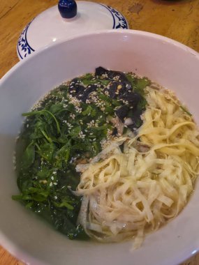 Sağlıklı dengeli yin yang eriştesi beyaz kâse içinde yeşil sebze ve susam tohumu. Lezzetli, taze öğle veya akşam yemeği için armoniyi simgeleyen iştah açıcı bir Asya yemeği.