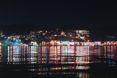 Geceleri sakin bir şehir silueti, durgun suya yansıyan canlı renkli bir ışık. Güzel şehir manzarası karanlık liman boyunca huzurlu ve huzurlu bir manzara yaratır.
