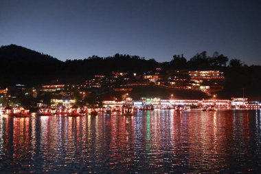 Huzurlu bir gece manzarası şehrin rıhtımını gösteriyor. Suyu yansıtan rengarenk bir ışık. Aydınlatılmış bina alacakaranlıkta canlı ve romantik bir atmosfer yaratır.