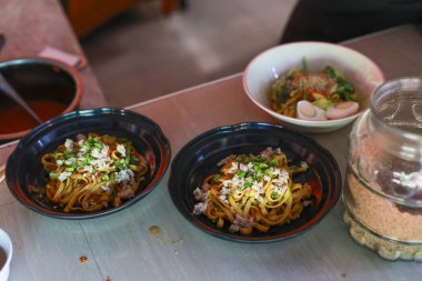 Lokanta tezgahında siyah kasede Asya eriştesi. Taze malzemeler, et ve lezzetli sosla nefis bir öğle yemeği iştah açıcı, otantik bir aşçılık deneyimi yaratıyor.