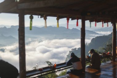Dağ manzaralı sakin bir sabah, siluette oturan insanlar bulutların üzerinde huzurlu bir güneşin doğuşunu izliyorlar. Asya 'daki ahşap balkonda sakin, düşünceli bir an.