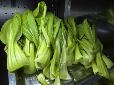 Taze bok choy, yeşil yapraklı sebze metal rafta yığılı. Sağlıklı yemek ve vejetaryen diyeti için çiğ Çin lahanası malzemesi. Hafif solmuş ve gevşek görünüyor.