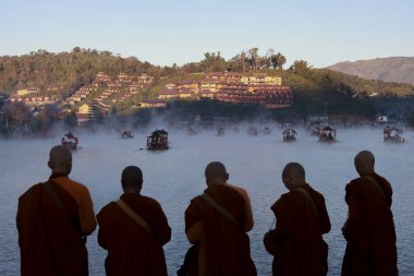 Beş Budist keşiş sisli gölün üzerinde huzurlu bir güneşin doğuşunu izliyor. Güneydoğu Asya 'da sakin, ruhani bir sabah sisli su ve uzak köy manzarasıyla.