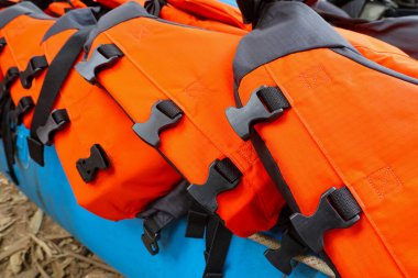 Mavi şişme botta siyah kayışlı parlak turuncu can yeleklerini yakından izleyin. Su sporu macerası için güvenlik ekipmanları, hazırlık ve beklenti ifade ediyor
