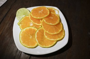 Beyaz tabakta taze dilimlenmiş portakal ve limonlu garnitür. Bu sağlıklı turunçgiller koyu ahşap masada sulu ve doğal C vitamini dolu olarak otururlar.