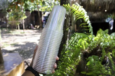 Parti için tek kullanımlık temiz plastik bardak destesi, yeşil doğa ve yeşillik arka planlı. Bir etkinlikte soğuk içecek servisi yapmaya ya da toplanmaya hazır.