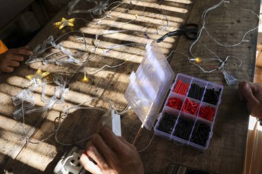 Odaklanmış elleri olan yaratıcı insanlar yıldız ışıklarıyla DIY tekneleri yapıyor ve kırsal ahşap masa üzerinde kablolar yapıyorlar. Güzel güneş ışığı ve gölgeyle aydınlatılmış işbirlikçi an