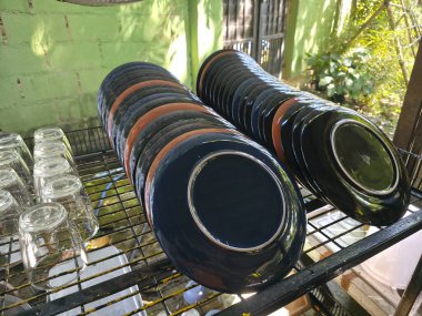 Dışarıdaki metal raflarda kuruyan siyah tabaklar ve temiz tabaklar. Bu sofra takımı ve mutfak eşyaları koleksiyonu tatmin edici düzen ve evcimenlik duygusunu gösteriyor.