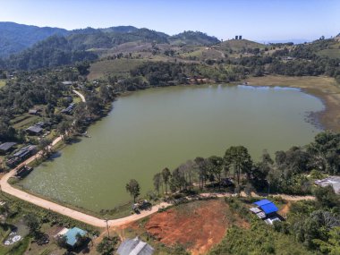 Sakin göl manzarası ve yeşil dağ vadisindeki küçük köy. Berrak mavi gökyüzü altında rezervuar, orman ve kırsal kesimin yer aldığı huzurlu bir manzara.
