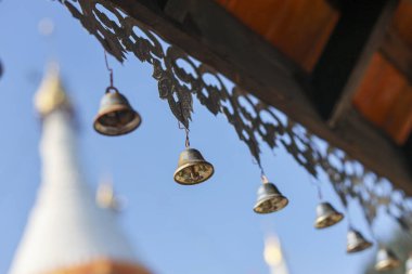 Asya 'daki süslü bir tapınak çatısından sarkan dingin pirinç rüzgâr çanı. Sakin arka plan açık mavi gökyüzünü ve pagoda 'yı gösteriyor, barışçıl ve ruhani duygular yaratıyor.