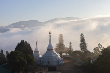 Tayland 'daki dağ manzarasının üzerinde sakin bir sabah güneşi doğuyor. manzaralı beyaz pagoda ve tapınak kompleksi bulut ve sis denizinden çıkar, huzur ve ruhani bir bakış açısı yaratır.