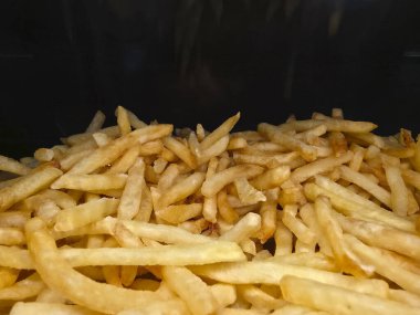 Altın patates kızartması yığını, klasik patates atıştırmalığı manzarası çok cazip. Bu gevrek, kızarmış, sağlıksız, siyah arka plandaki fast food yemeye hazır görünüyor.