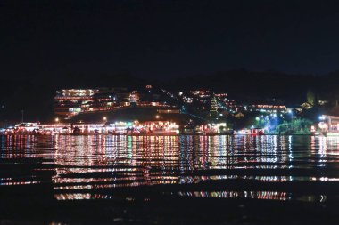Tepedeki parıldayan köyün huzurlu gece manzarası. Karanlık suları yansıtan renkli bir ışık. Bu huzurlu şehir manzarası güzel ve huzurlu manzaralar sunuyor.