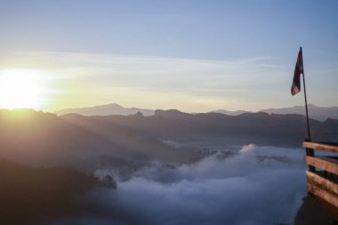 Sis denizi ile birlikte dağ manzarasının üzerinde huzurlu bir sabah güneşi doğuyor. Manzaralı manzaralı bayrak vadi manzarası ve güzel altın güneş ışığı sunuyor.