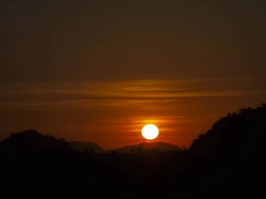 Dağ siluetinin arkasında güzel turuncu güneş batıyor. Sakin gökyüzü huzur dolu bir ışıkla parlar, huzur dolu ve sakin bir arka plan yaratır, alacakaranlıkta