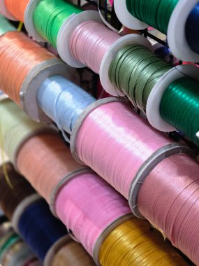 Askıdaki parlak kurdele makaralarından canlı ve renkli bir koleksiyon. Bu el işi, dikiş ve dekorasyon malzemelerinin çeşitliliği yaratıcılık duygusunu çağrıştırıyor.