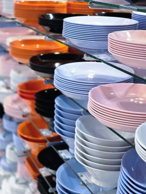 Vitrindeki cam raflara düzgünce istiflenmiş renkli plastik tabakların ve kaselerin düşük açılı görüntüsü. Bu mutfak malzemeleri çok çeşitli ve satılık ürünler sunuyor.