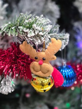 Kırmızı şapkalı ve zilli neşeli ren geyiği süsü şenlikli bir Noel ağacına asılmış, Noel ağacı dallarıyla süslenmiş. Tatil sezonu için sevimli dekorasyon manzarasını kapat