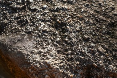 Sert taş yüzeyi doğal granit kaya dokusunu gösteriyor. Kahverengi ve gri mineral arkaplanlı jeoloji deseninin yakından incelemesi katı ve dünyevi bir his yaratıyor.