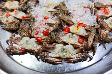 Parlak turuncu kabuklu taze mavi yengeç ve ezilmiş buzlu vişneli domates. Marketteki metal kasenin içindeki lezzetli deniz ürünleri malzemelerini kapatın.