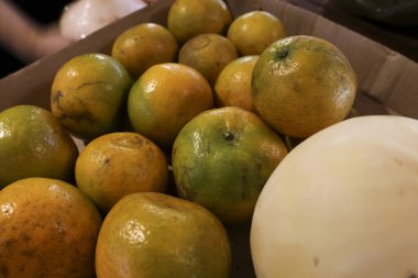 Kutuda yığılmış taze yeşil ve sarı portakalların yakın görüntüsü. Doğal turunçgiller, sağlıklı beslenme ve organik besinleri temsil ederek pazarda satışa sunulmaya hazırdır.