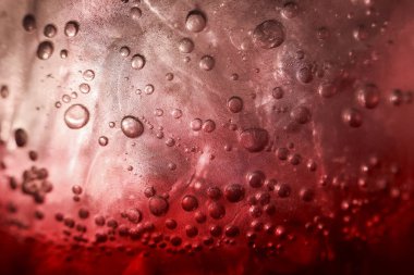 Buz küpü ve karbonatlı baloncukla soğuk kırmızı içeceğin ferahlatıcı görüntüsü. köpüren sıvının makro görünümü yaz arkaplanı için soyut bir dokuyu gösterir