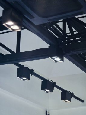 Parlak spot ışıklarıyla modern siyah pist aydınlatmasının düşük açılı görüntüsü. İç tavan üzerindeki endüstriyel metal yapısı, minimalist tasarım için odaklanmış, çarpıcı bir aydınlatma sağlıyor