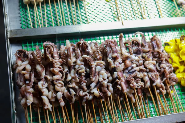 Canlı gece pazarında şiş üstünde çiğ mürekkep balığı. Asya sokak yemekleri, taze deniz ürünleri, kızartılmayı bekliyor. Yerel yemek dükkanından popüler ve lezzetli aperatifler